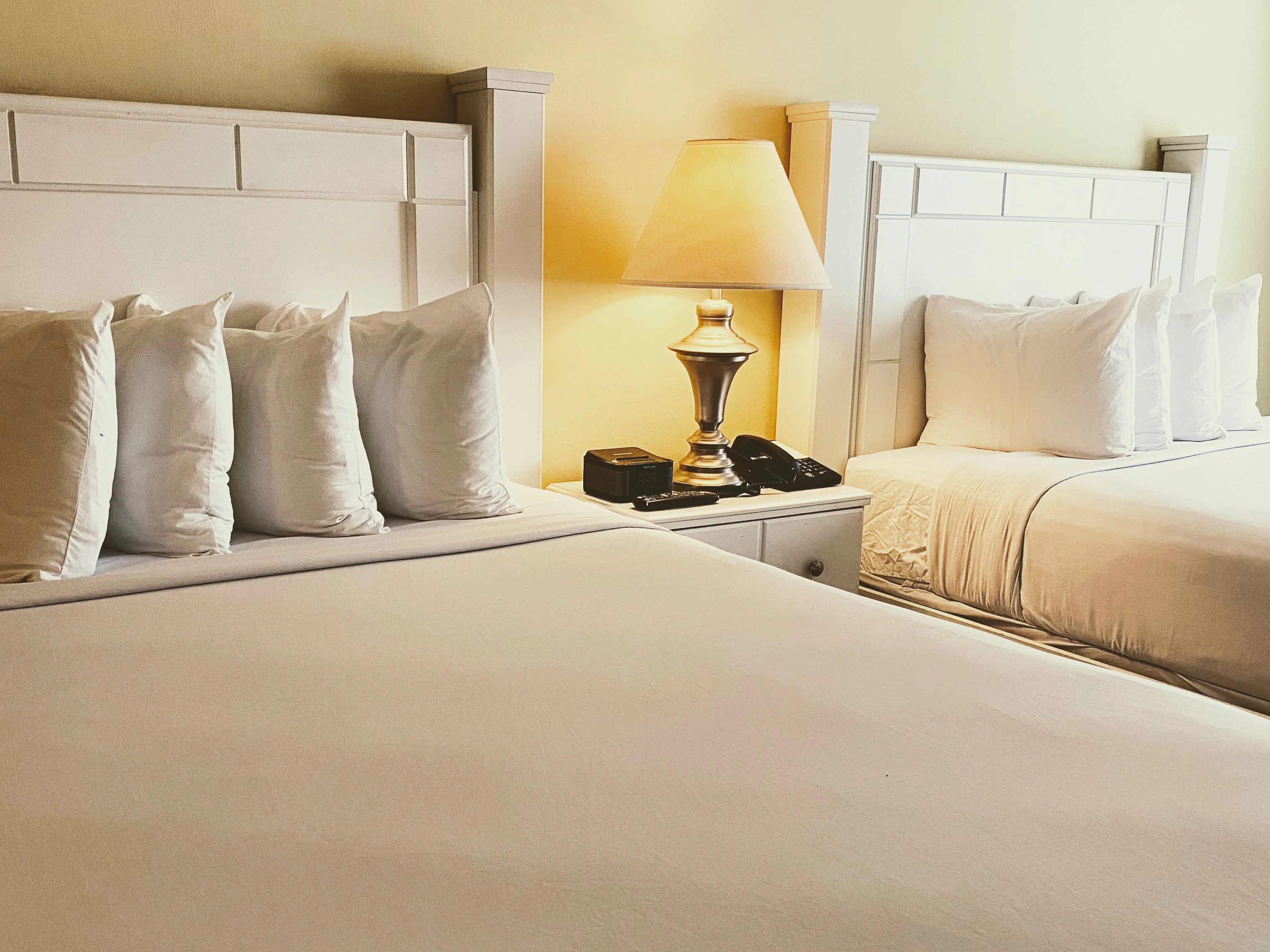 A close-up of two white beds with pillows and a lamp on a nightstand.