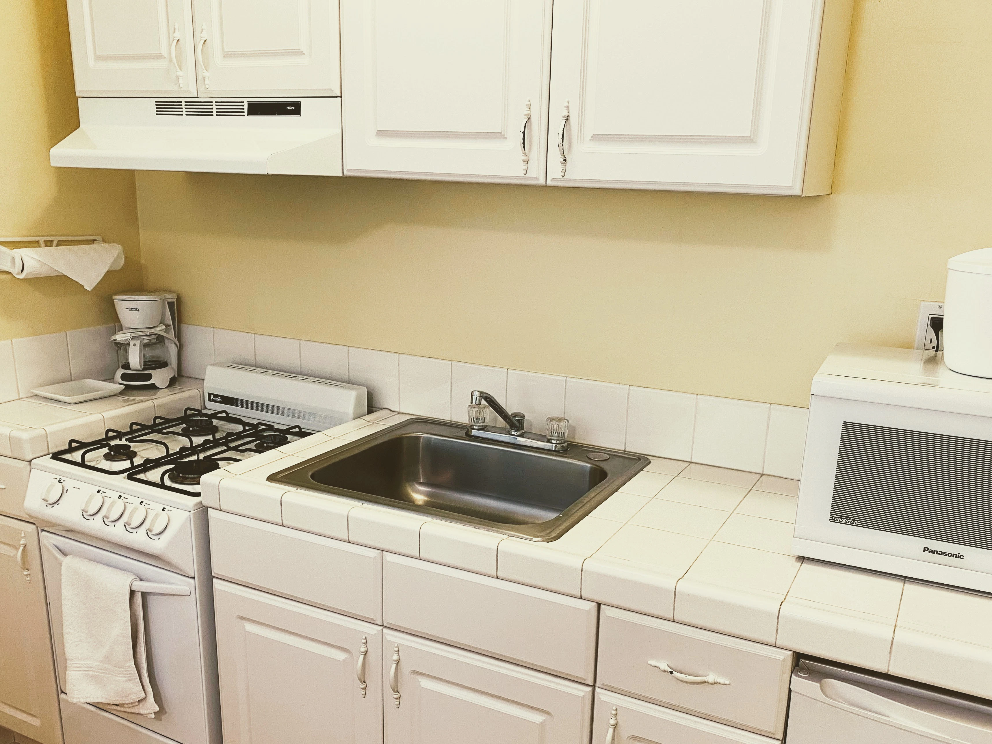 A kitchenette with white cabinets, stainless steel sink, and white appliances.