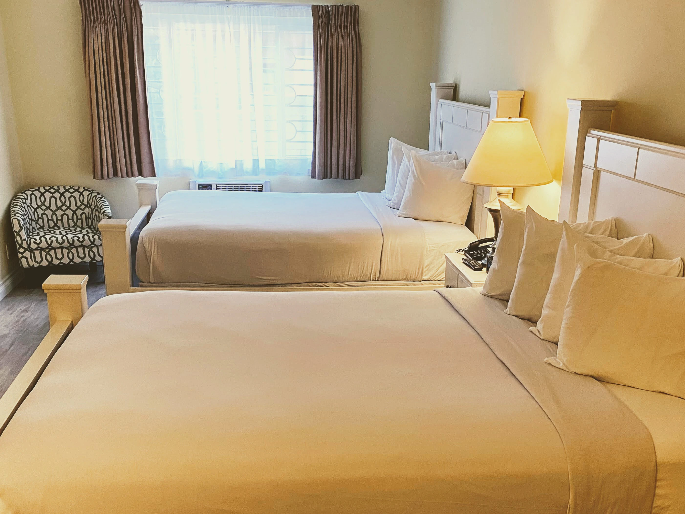 A hotel room with two beds, a chair, and a window.