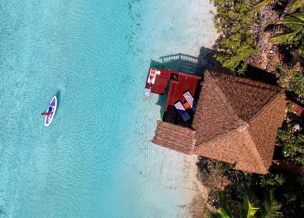 Aitutaki Island, Cook Islands, Overwater Bungalow Guest paddleboarding on the clear waters of Aitutaki Lagoon